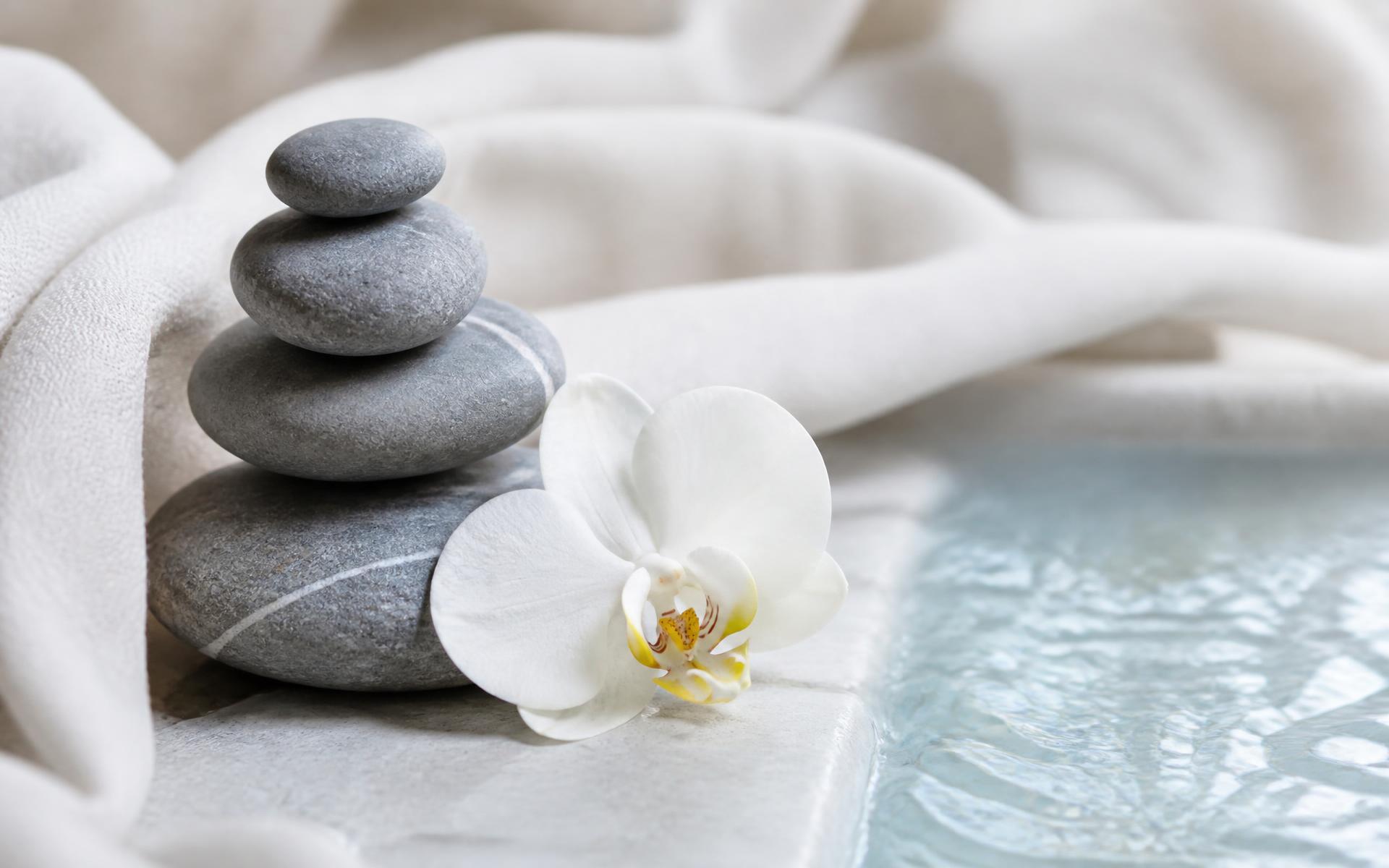 Smooth massage stones beside a white orchid and clear blue water